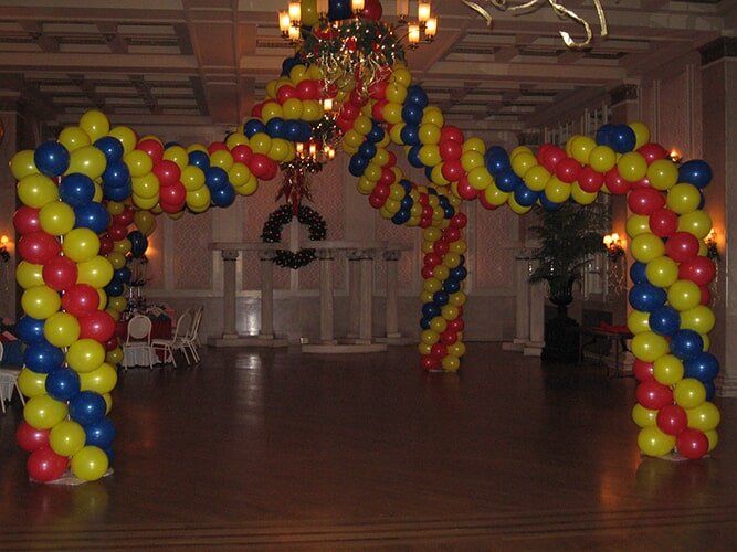 Balloon arch in yellow, blue, and red over a doorway inside a building.