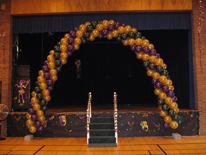 Balloon arch in gold, purple, and black over a stage with steps, decorated for an event.
