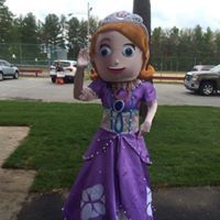 Sofia the First character in a purple dress costume waving outdoors near a parked car.