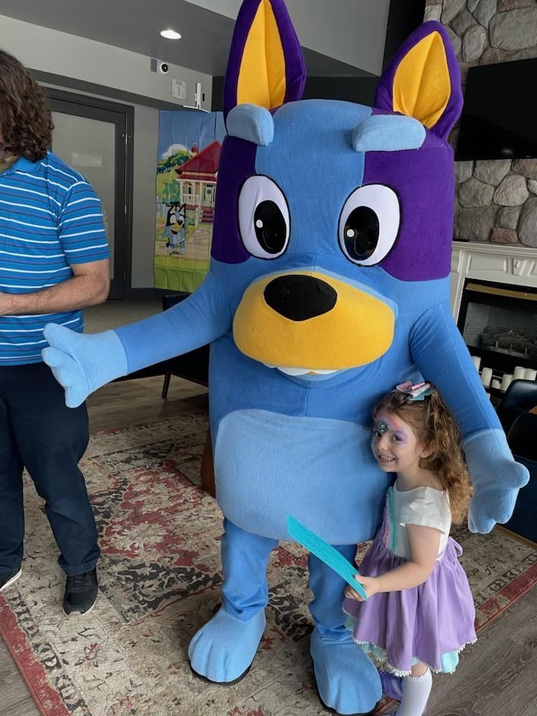 Bluey mascot with a child, inside, by a fireplace.