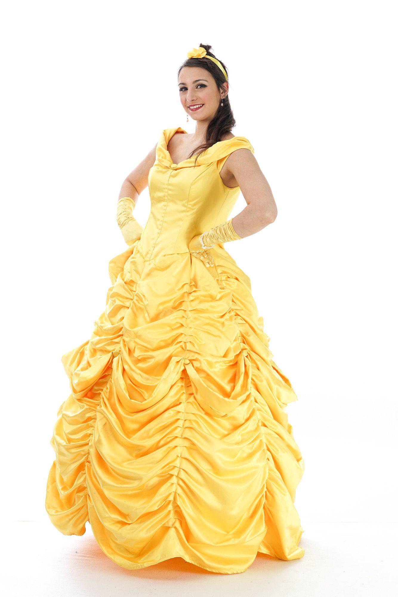Woman in a yellow ballgown, posing with hands on hips, smiling. White background.