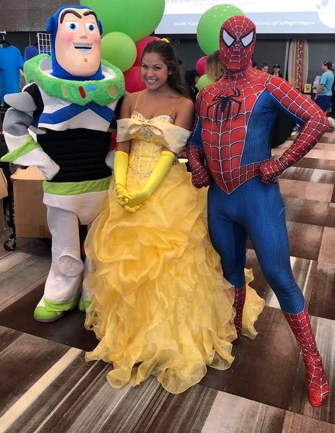 Buzz Lightyear, Belle, and Spider-Man posing together. Woman in yellow gown, balloon backdrop.