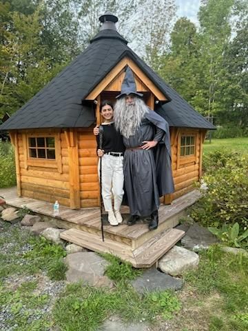 Person in wizard costume poses with a person in front of a wooden cabin.