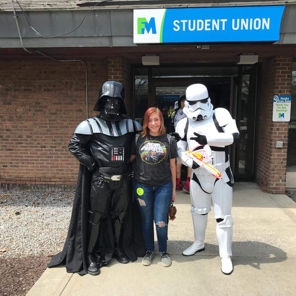 Woman poses with Darth Vader and Stormtrooper outside a student union building.