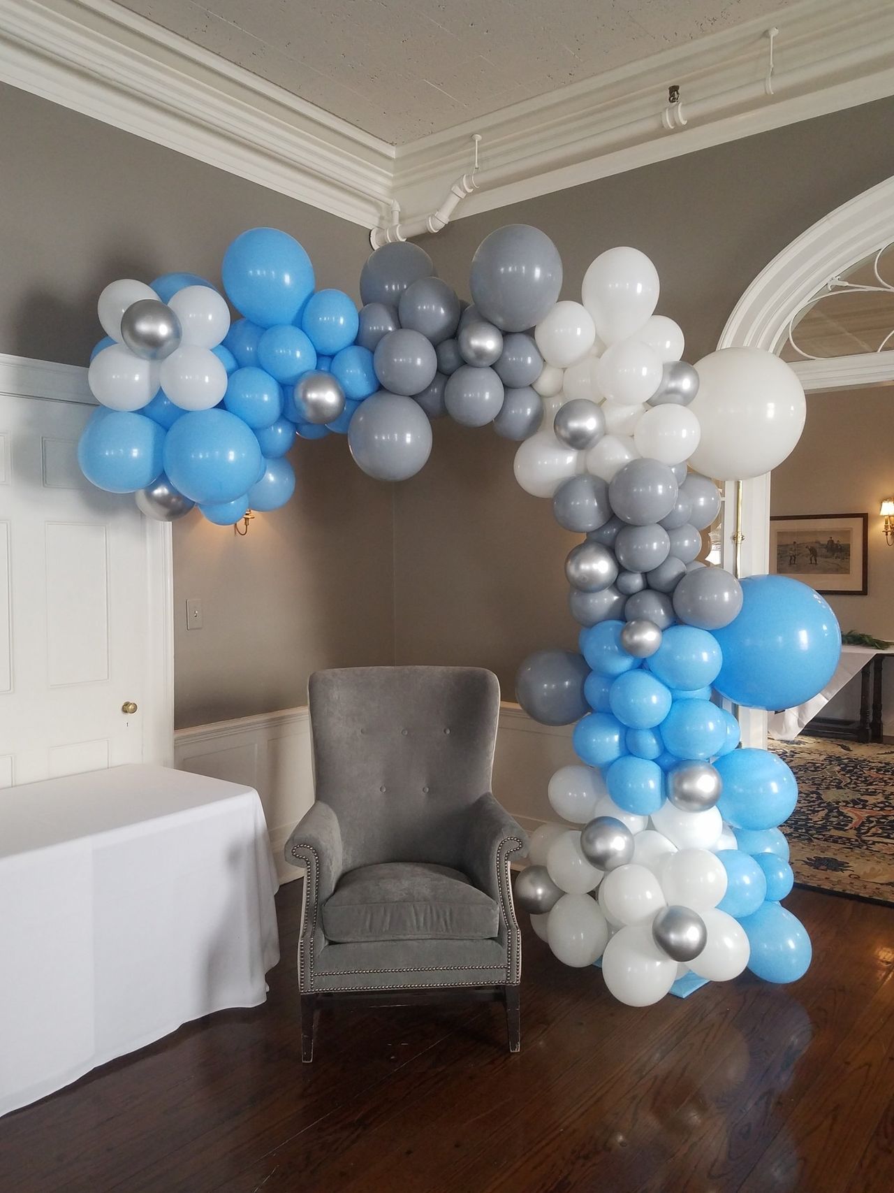 Balloon arch in blue, gray, and silver colors frames a gray armchair.