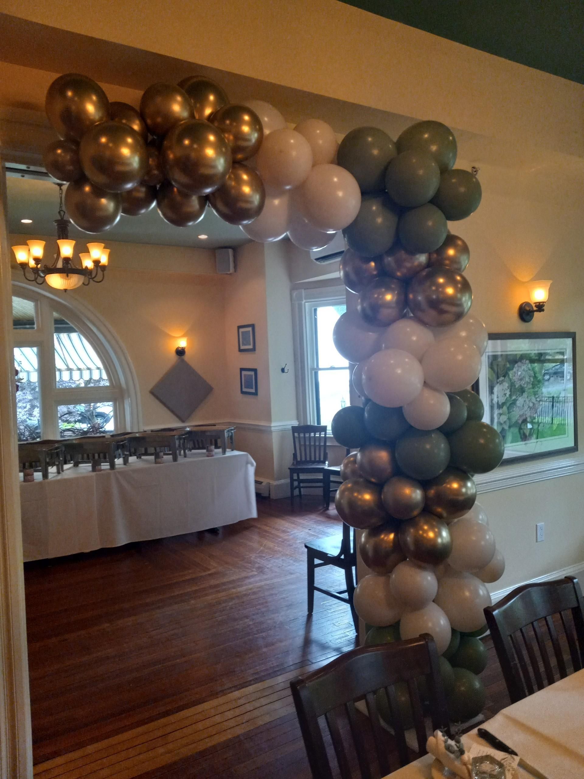 Archway decorated with gold, white, and green balloons, likely for an event at a restaurant.