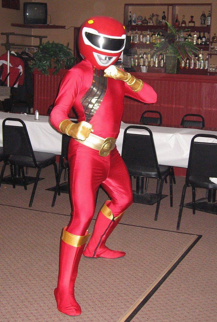 Red Power Ranger in fighting stance, in a room with tables and chairs.