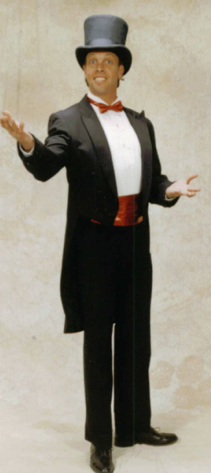 A man in a tuxedo, top hat, and red cummerbund, with arms outstretched in front of a neutral backdrop.