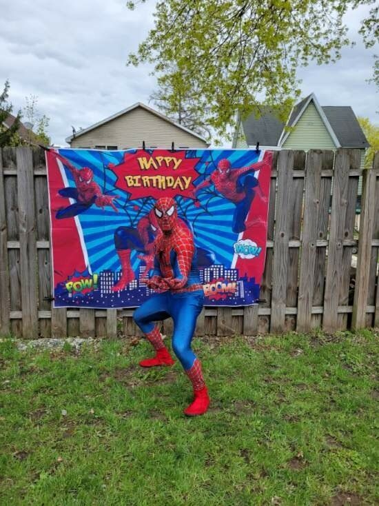 Person in Spider-Man costume poses in front of a birthday banner on a wooden fence.