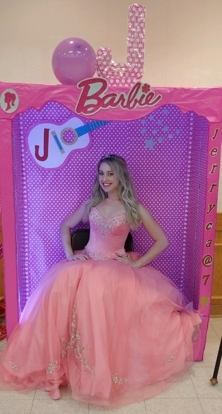 Woman in a pink gown poses in front of a Barbie-themed backdrop.