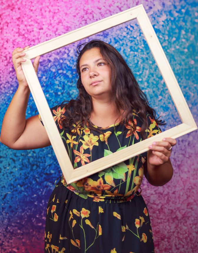 Woman holding a wooden frame against a pink-and-blue textured backdrop
