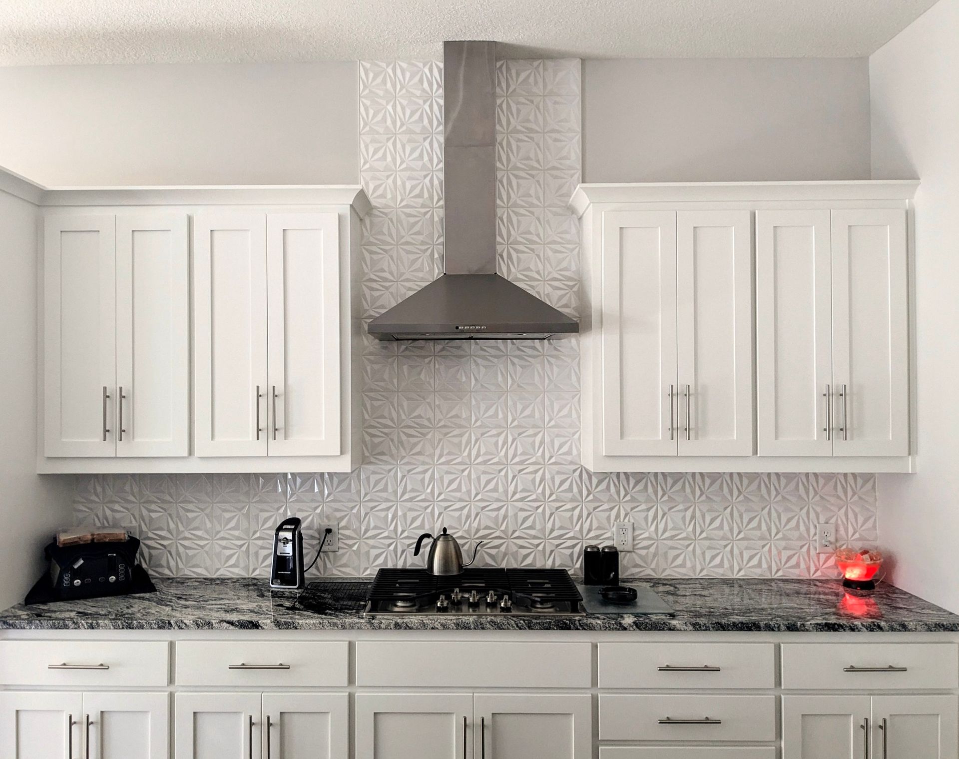 A kitchen with white cabinets , granite counter tops , a stove and a hood.