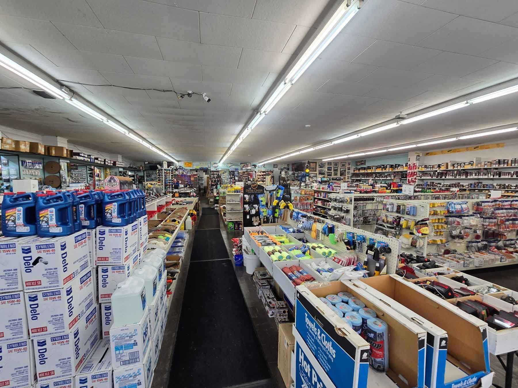 Interior view of a well-stocked store aisle, with shelves filled with various items, including oil and tools.