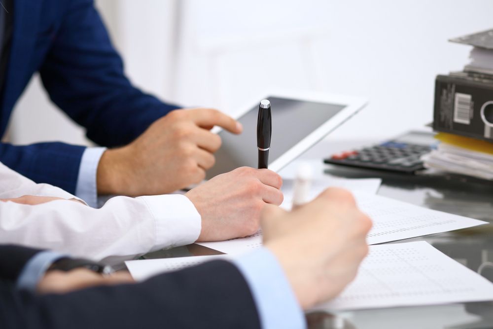 People in business attire taking notes at a meeting table with a tablet and calculator — Qwerty Plus in Newcastle, NSW
