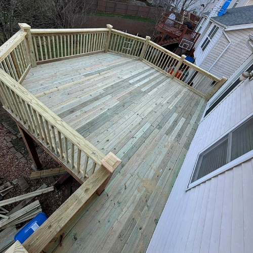 Newly built wooden deck with railing attached to a white house.