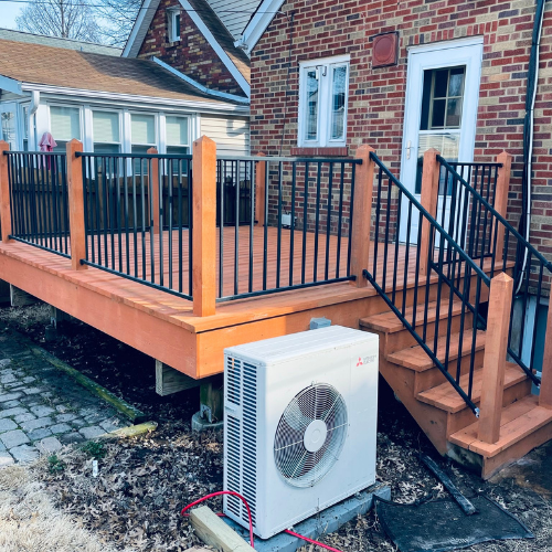 A backyard deck with black railing next to a brick house and an air conditioning unit.