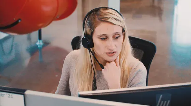 Woman wearing a headset working at a desk with two monitors in an office setting