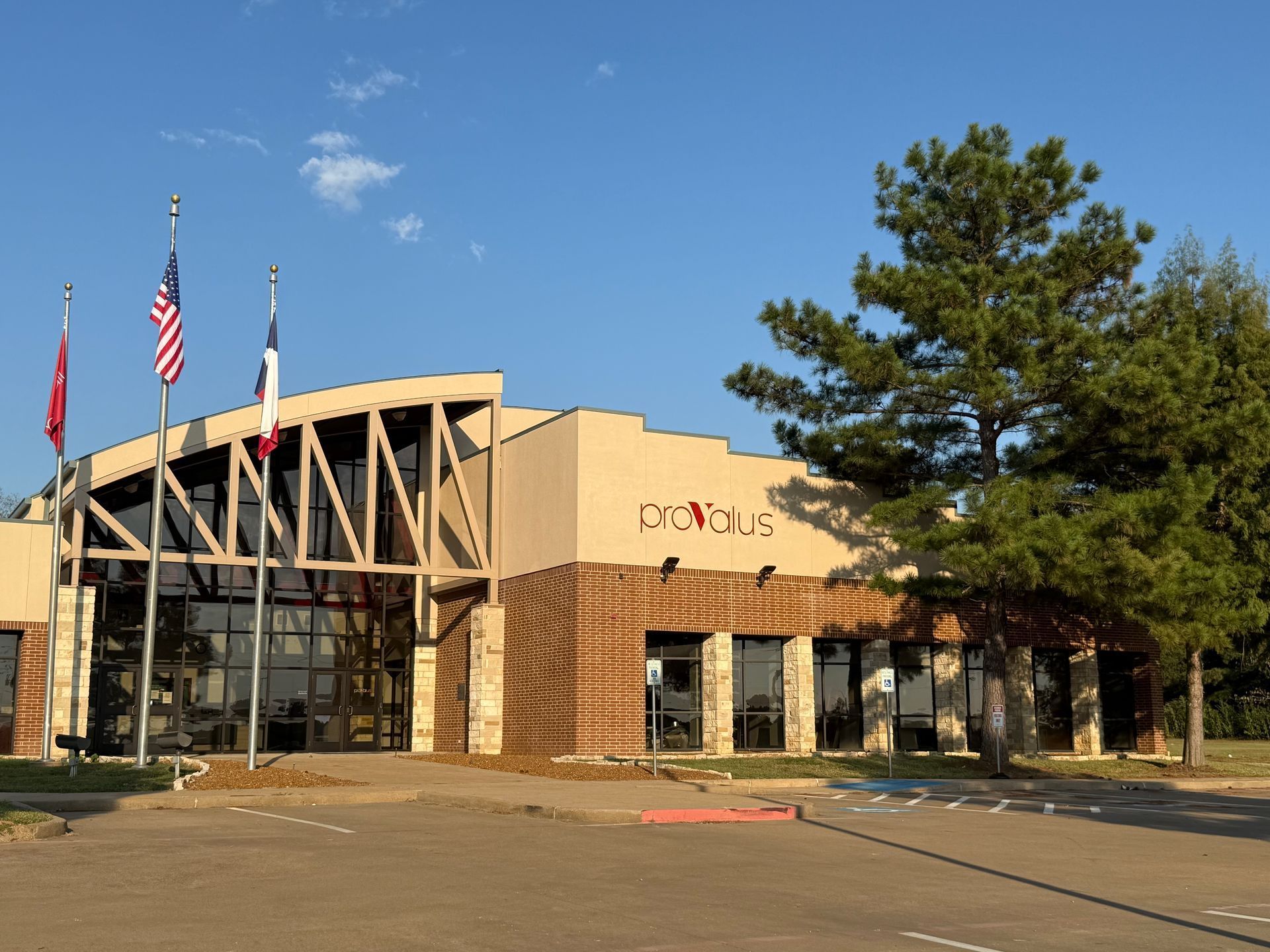 Library building with brick facade, glass entrance, flags, and a large tree under a blue sky