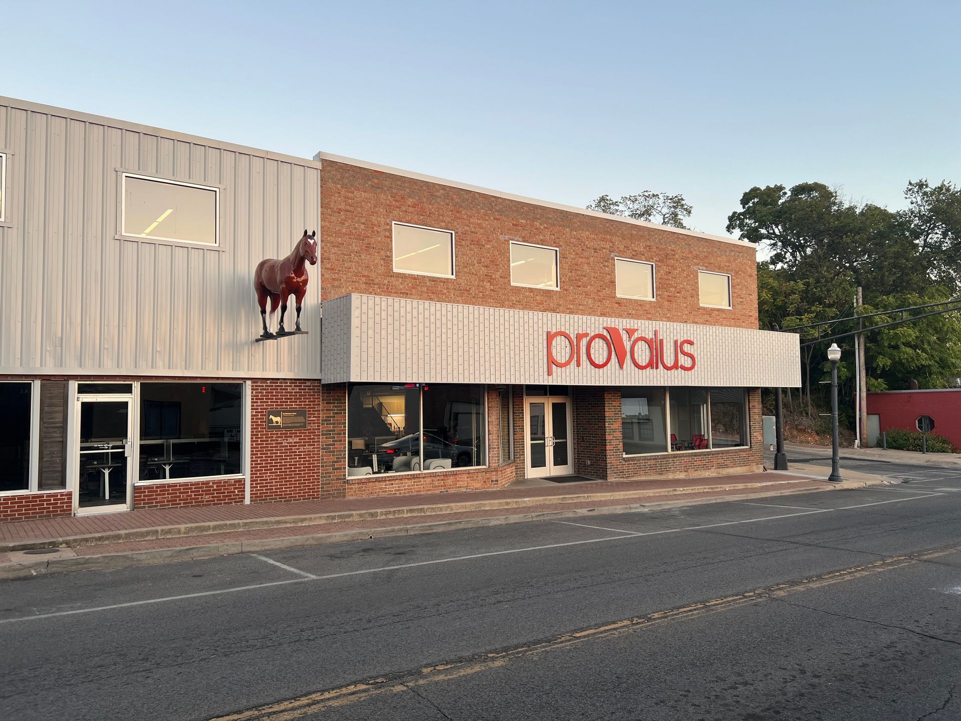 Street view of a brick storefront with a red Proxus sign and a horse statue on the facade
