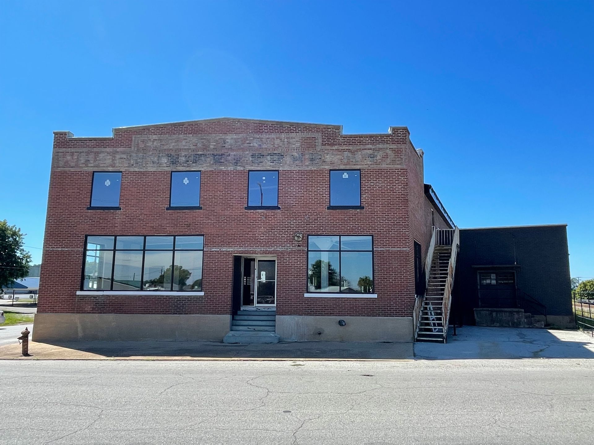 Red brick storefront with large windows and metal stairs on the right under a clear blue sky