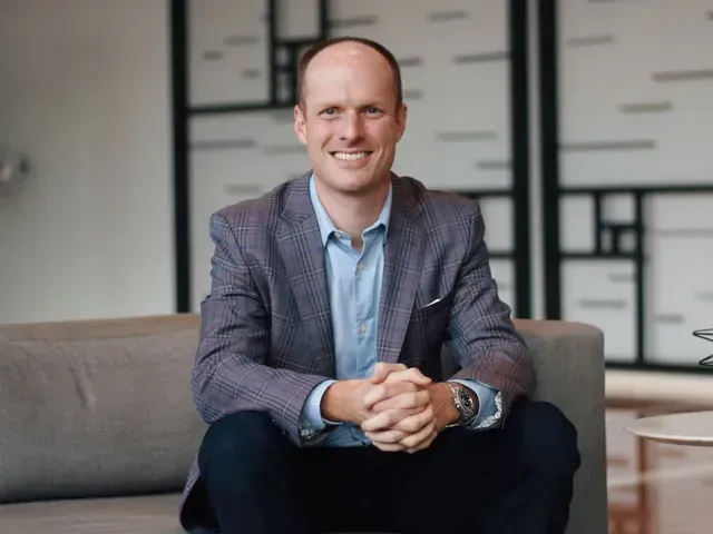 Smiling man in a gray blazer sitting on a couch in a modern office lobby