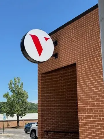 White circular storefront sign with a red V on a brick building against a blue sky.