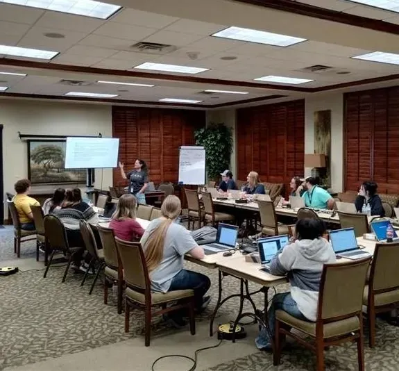 Conference room training session with people seated at tables facing presenters and whiteboards