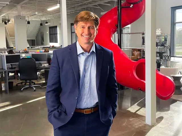 Man in blue suit smiling in a modern office beside a bright red slide