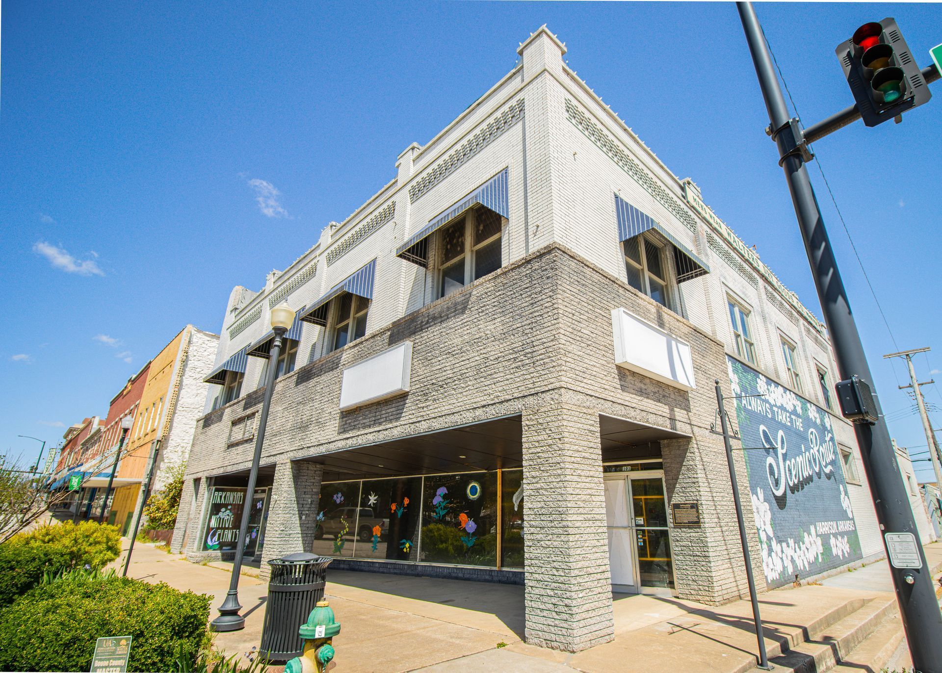 Corner storefront building with stone facade, large windows, and a traffic light on a sunny street corner