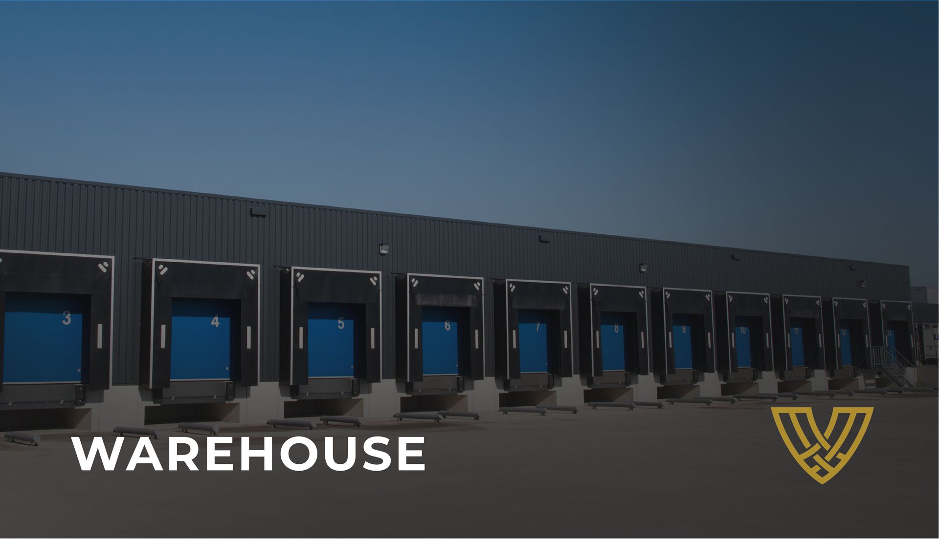 A row of blue loading dock doors on a dark gray warehouse building against a clear sky.