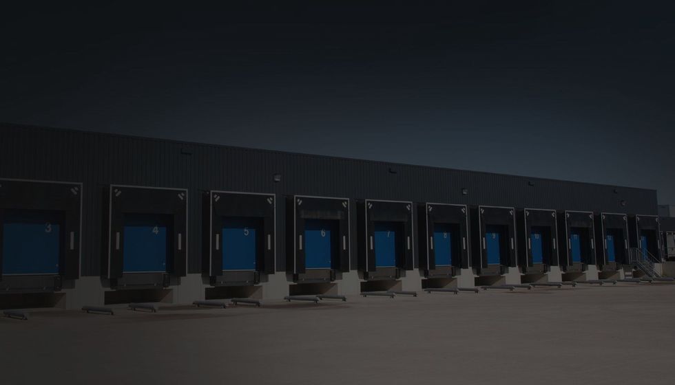 A row of shipping loading docks with blue door seals against a dark metal industrial building at dusk.
