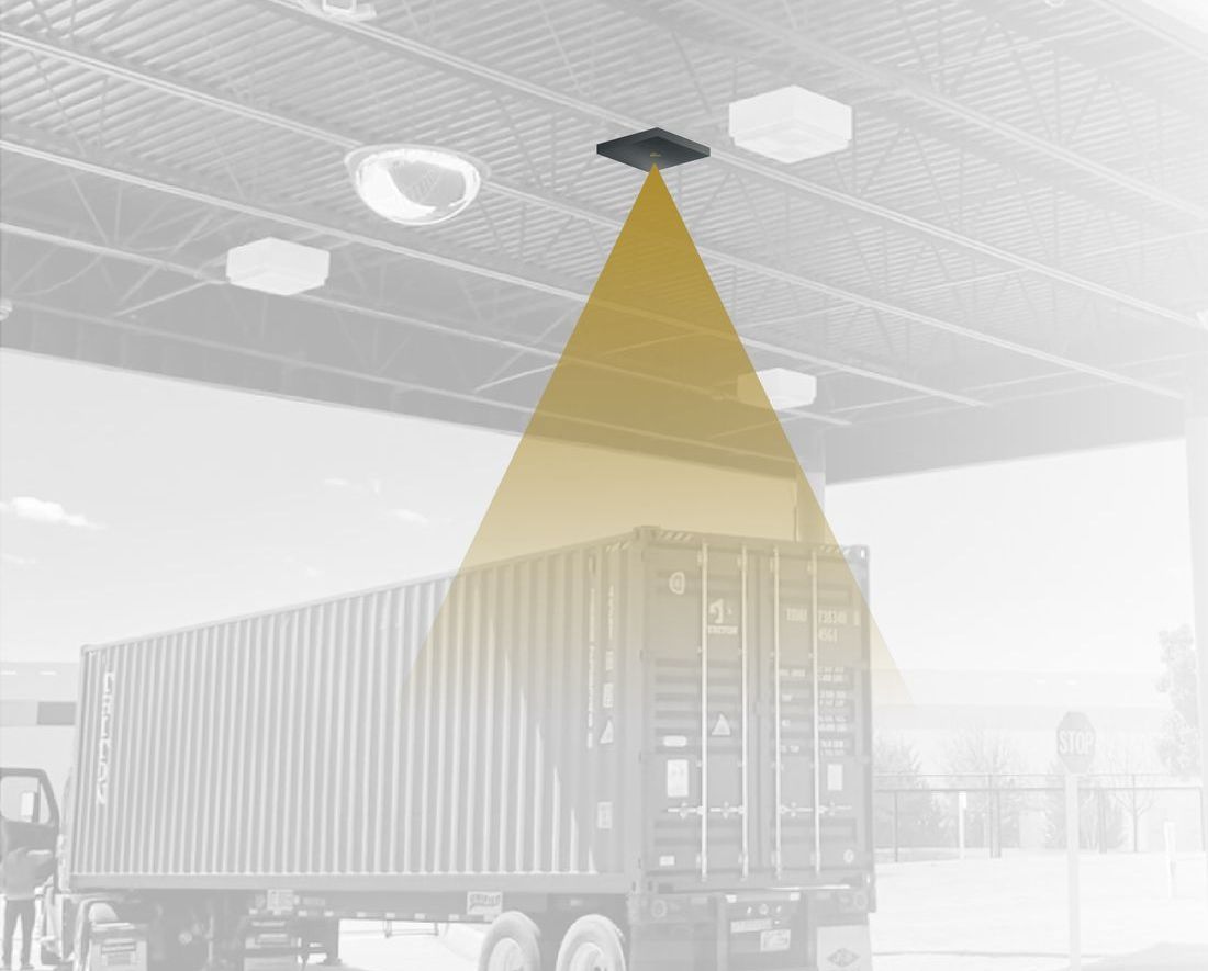 A ceiling-mounted sensor casts a cone of light over the top of a shipping container on a truck.