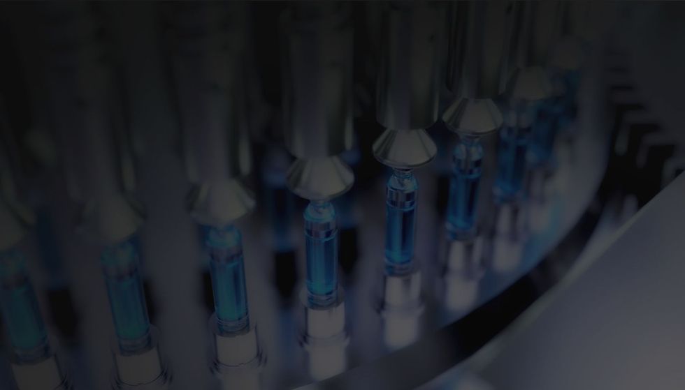 A machine filling a row of small glass vials with a blue liquid in an industrial pharmaceutical setting.