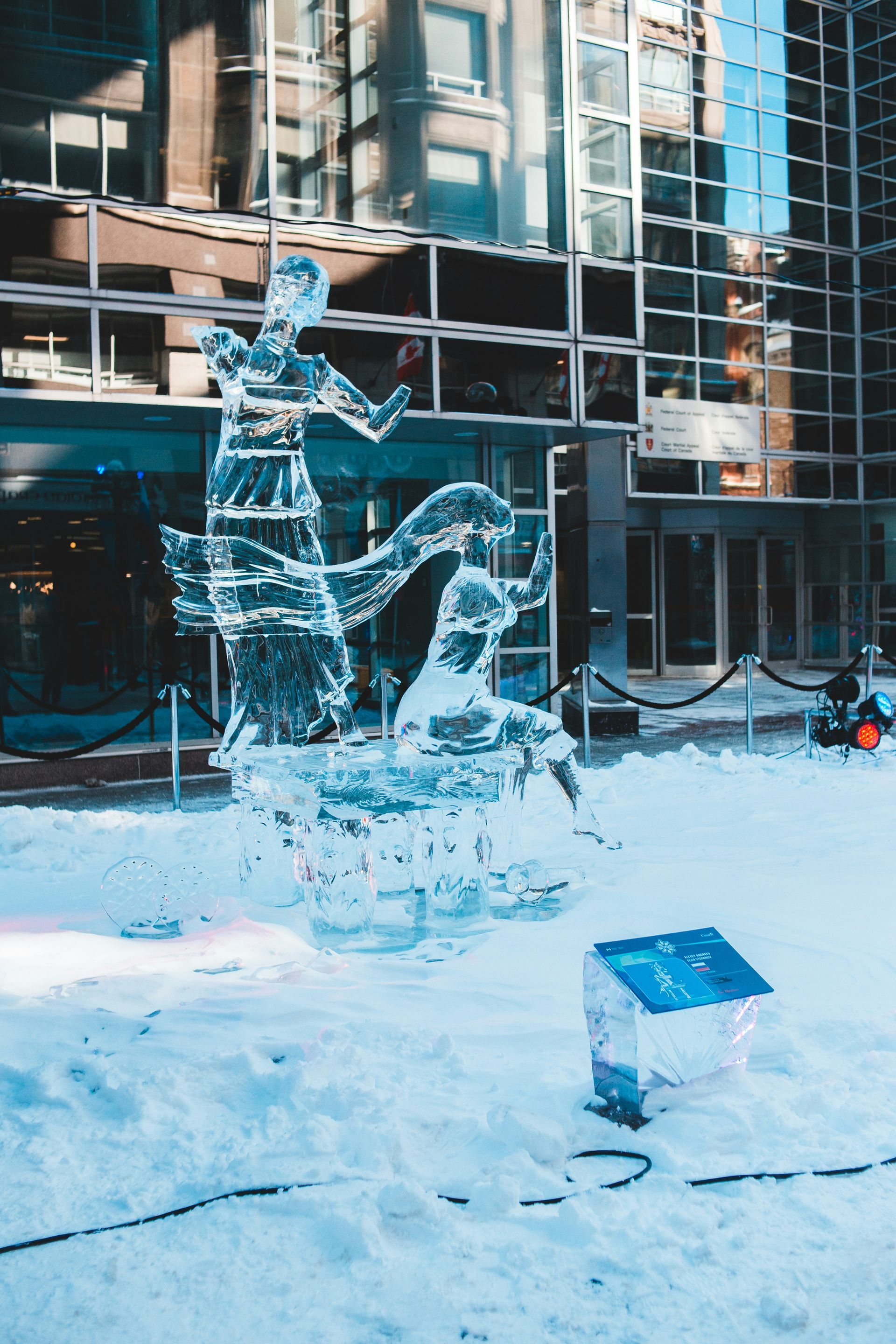 Scultura di ghiaccio raffigurante figure all'esterno di un edificio. Terreno innevato.