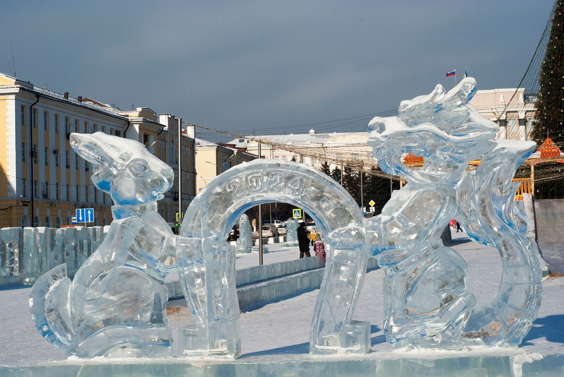 Scultura di ghiaccio raffigurante un drago in una piazza cittadina; tra i dettagli si notano un arco e del ghiaccio trasparente.