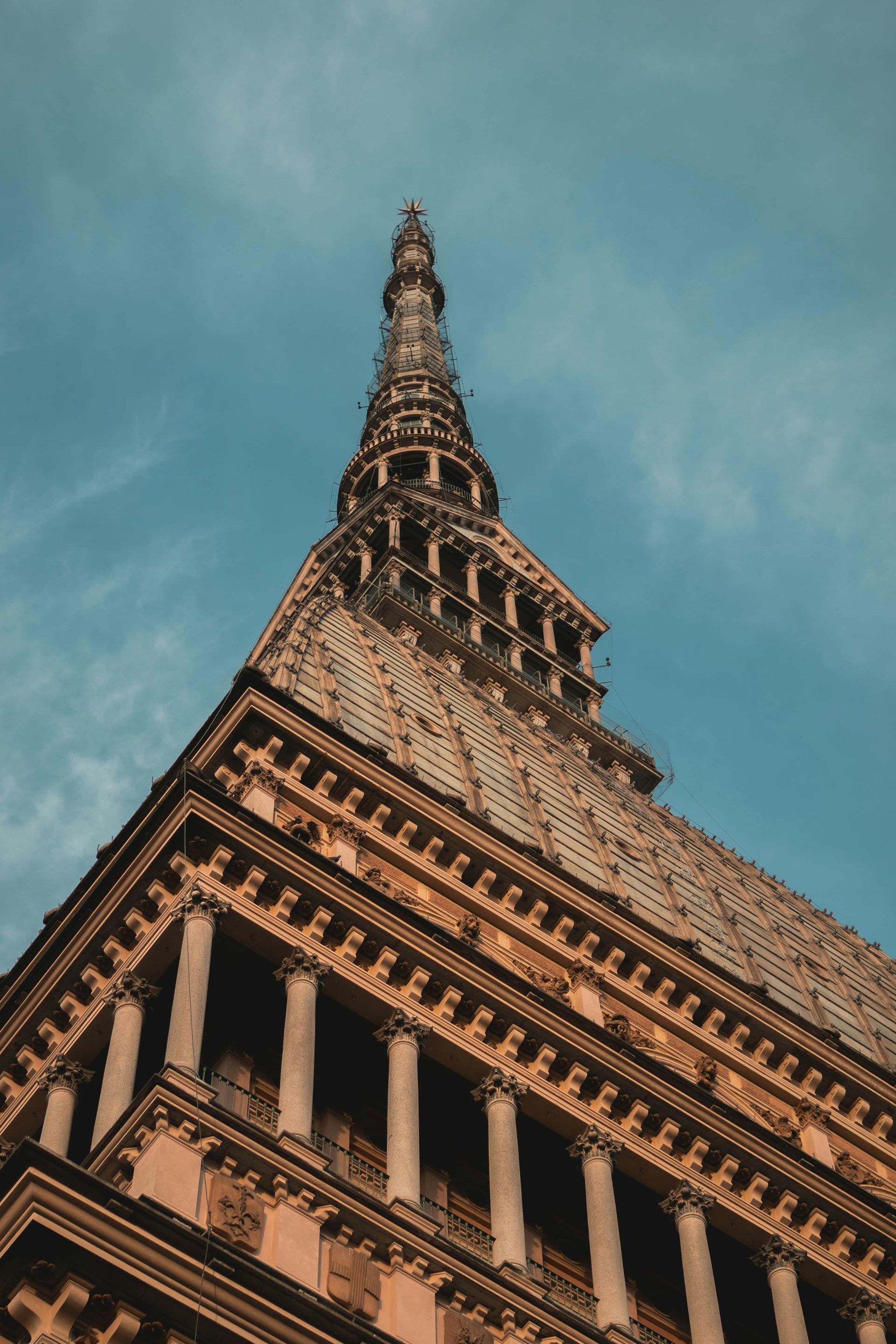 Vista dal basso della Mole Antonelliana a Torino, Italia. L'edificio ha un'alta guglia, che si staglia contro un cielo azzurro.