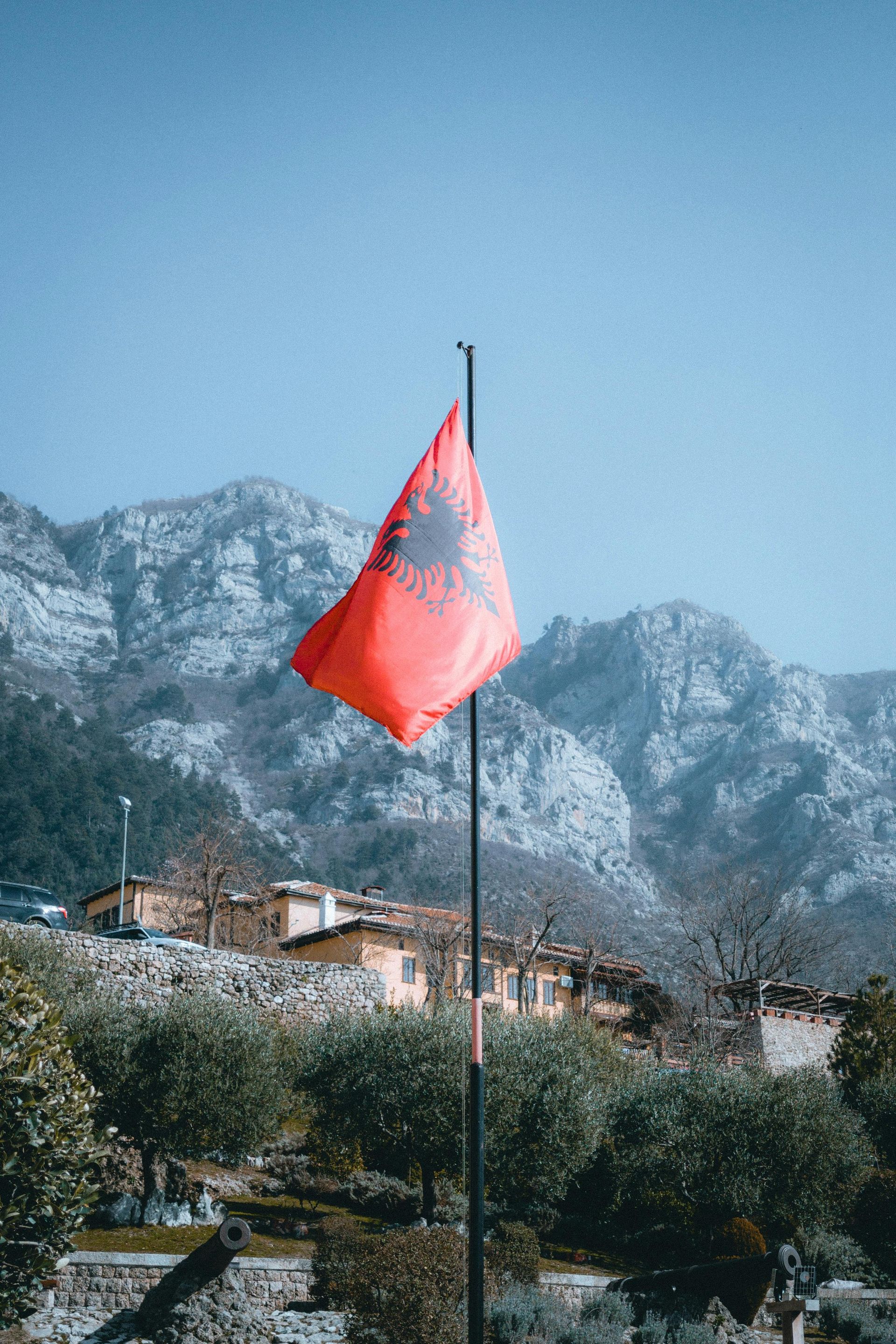 Una bandiera rossa dell'Albania sventola nel vento davanti a una montagna.