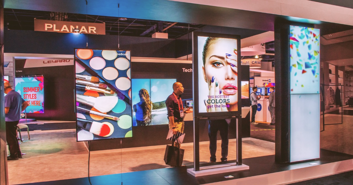LED display booth with illuminated digital screens and two people walking past in a mall-like setting