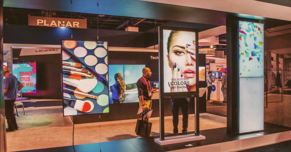People standing outside a Planar display showroom with colorful digital screens and posters