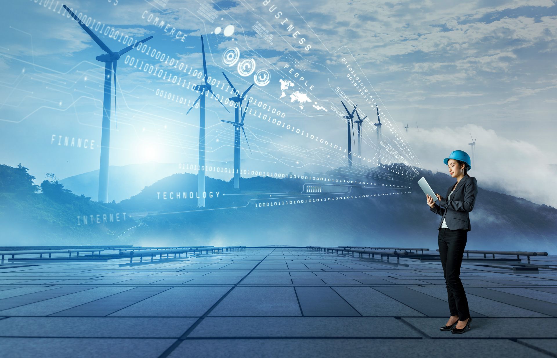 Engineer in hard hat using a tablet beside wind turbines and solar panels in a blue futuristic energy landscape