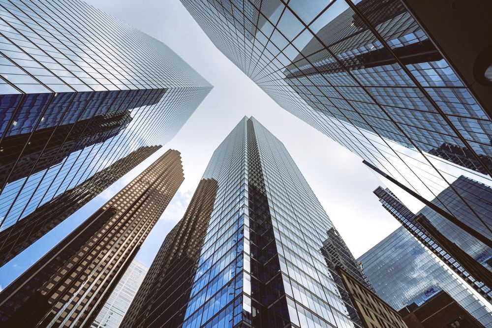 Skyscrapers shot from below, with glass facades converging toward a bright sky.