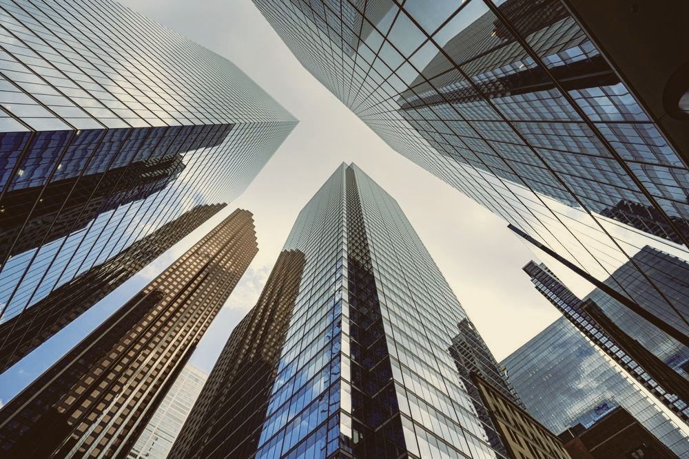 Upward view of glass skyscrapers converging against a bright sky