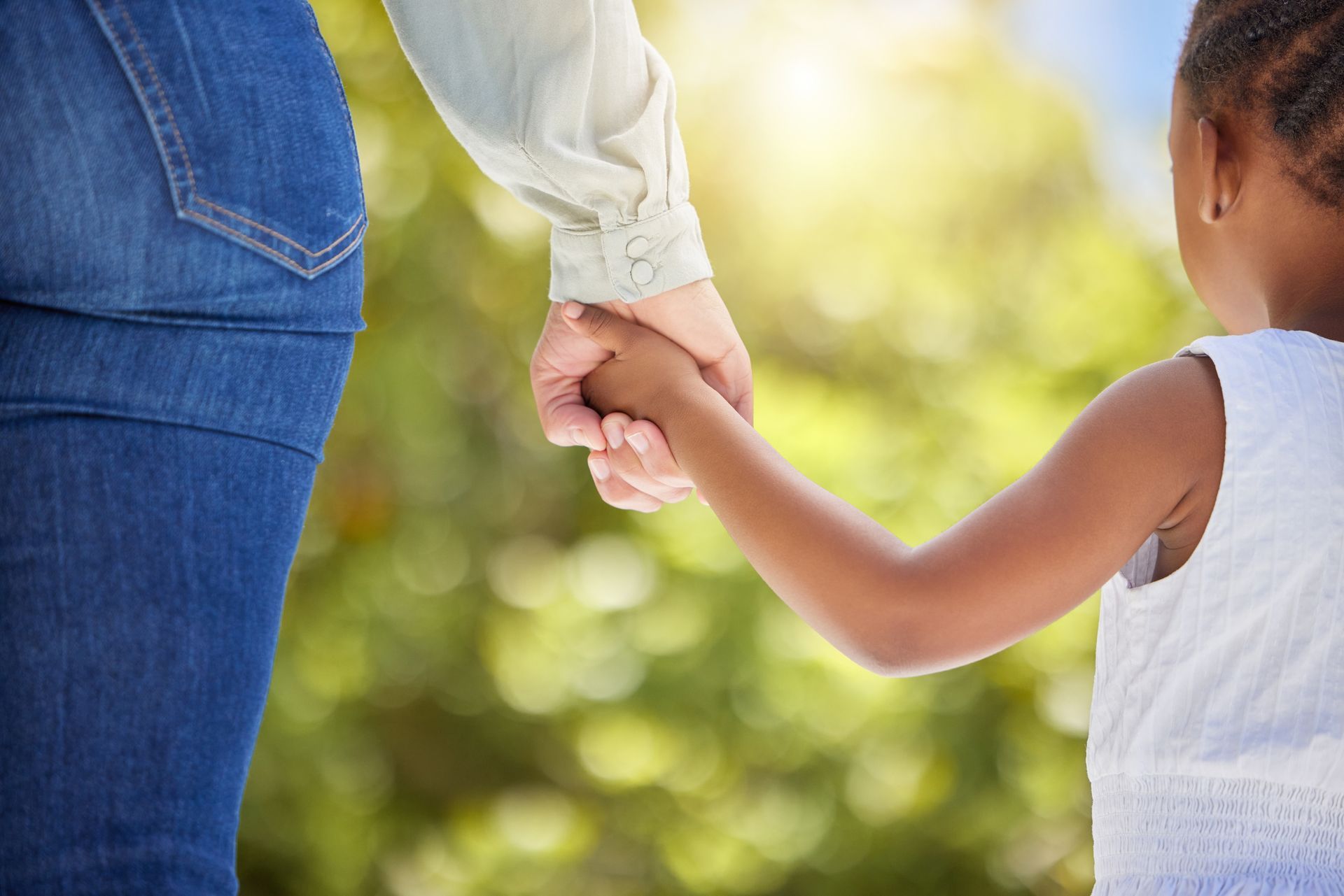 Two people holding hands outdoors, with a blurred green background