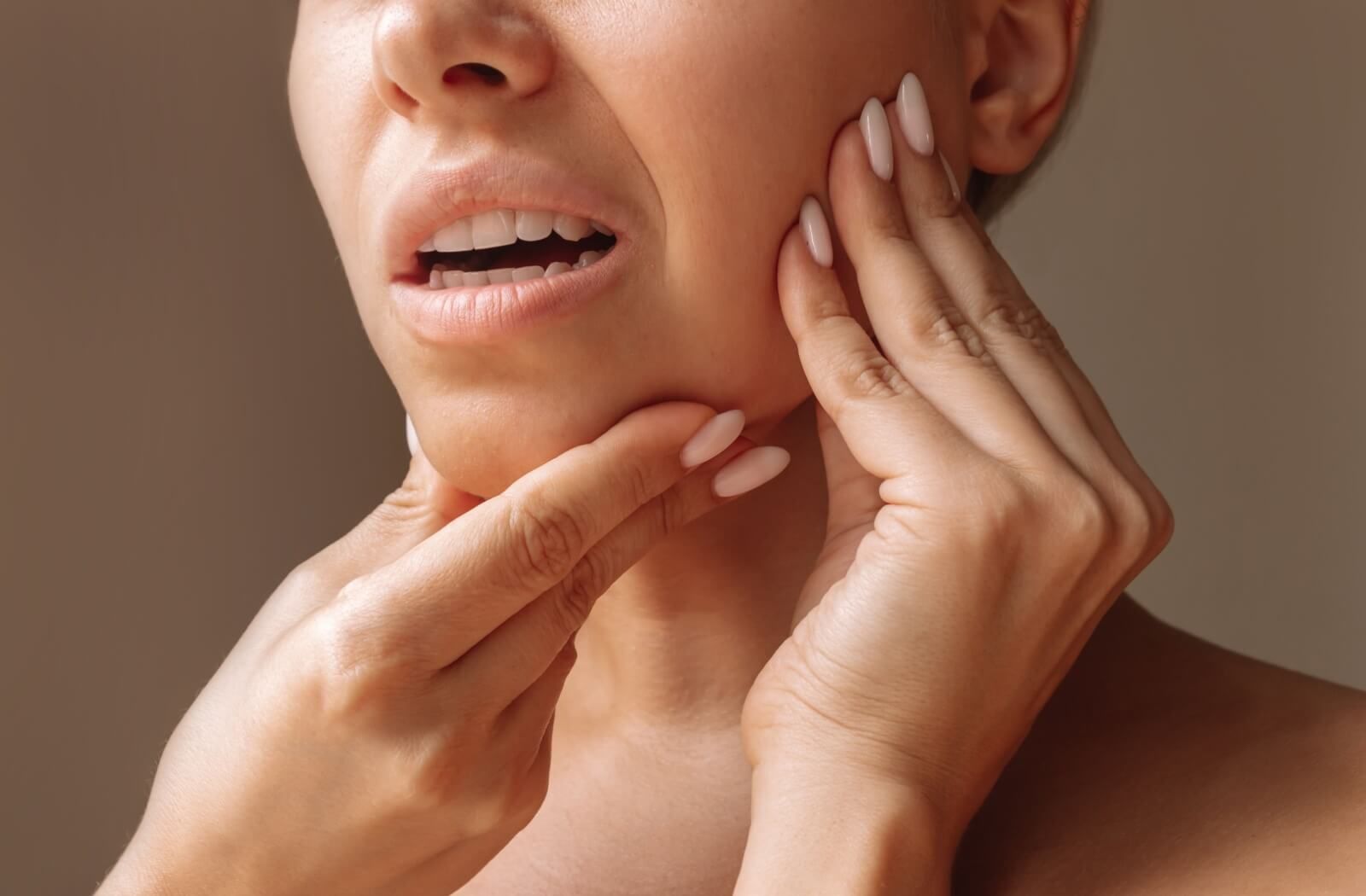 A close-up of a woman touching her jaw and chin with a pained expression, illustrating symptoms of TMJ disorder or jaw popping discomfort.