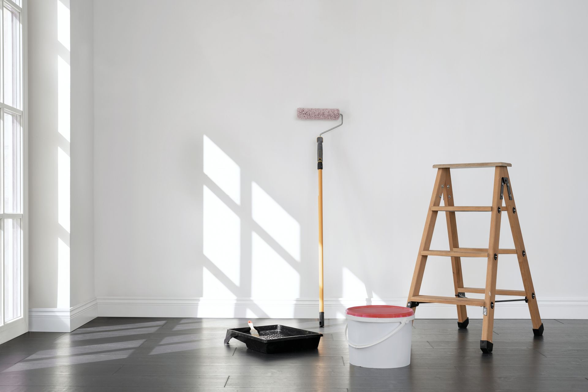 An empty room with a ladder , paint roller , and bucket of paint.