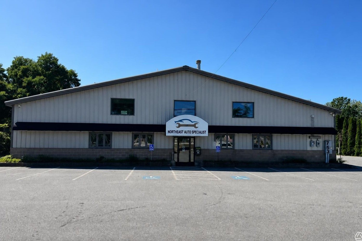 White community building with a peaked roof, central entrance, and wide gravel lot under a blue sky