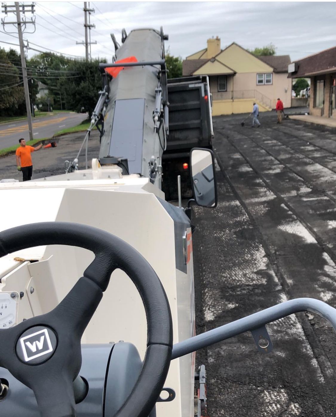 Roadwork with an asphalt paver and dump truck spreading fresh blacktop on a street, workers nearby