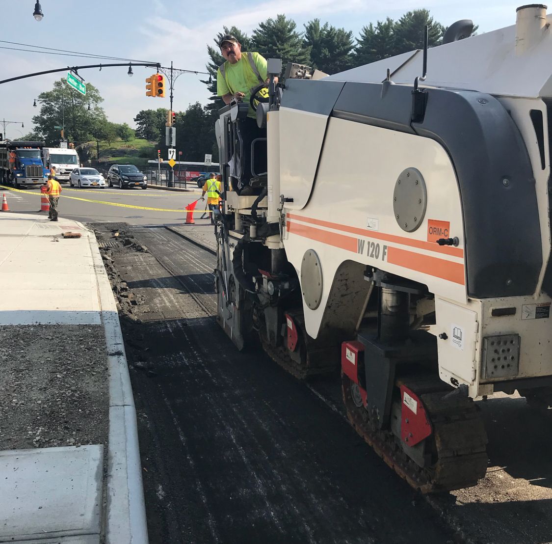 Street repair crew on a road paver laying fresh asphalt beside traffic cones at an intersection