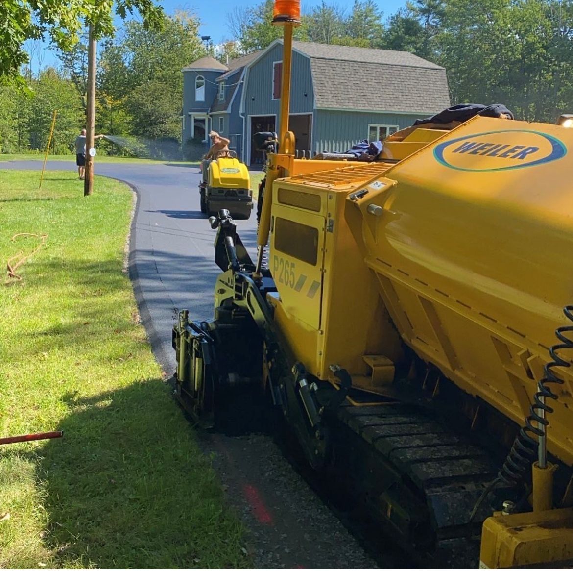 Yellow roadwork machine on a suburban street beside a house and lawn