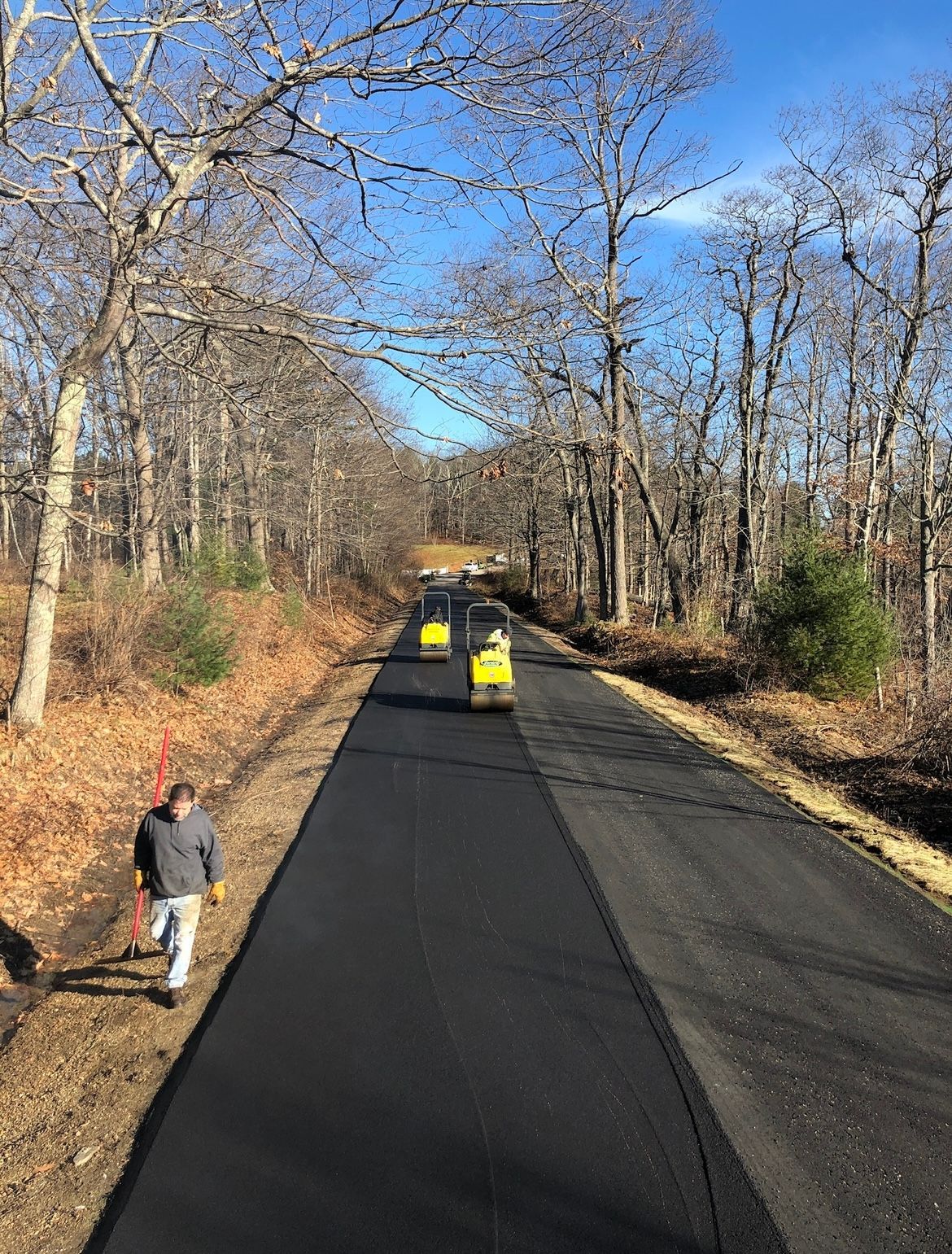 Paved road under construction with two yellow rollers and a person walking on the left side.